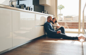 Young man and woman sitting on floor in kitchen and talking.