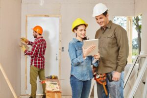 man and woman look at clipboard while renovator works in background