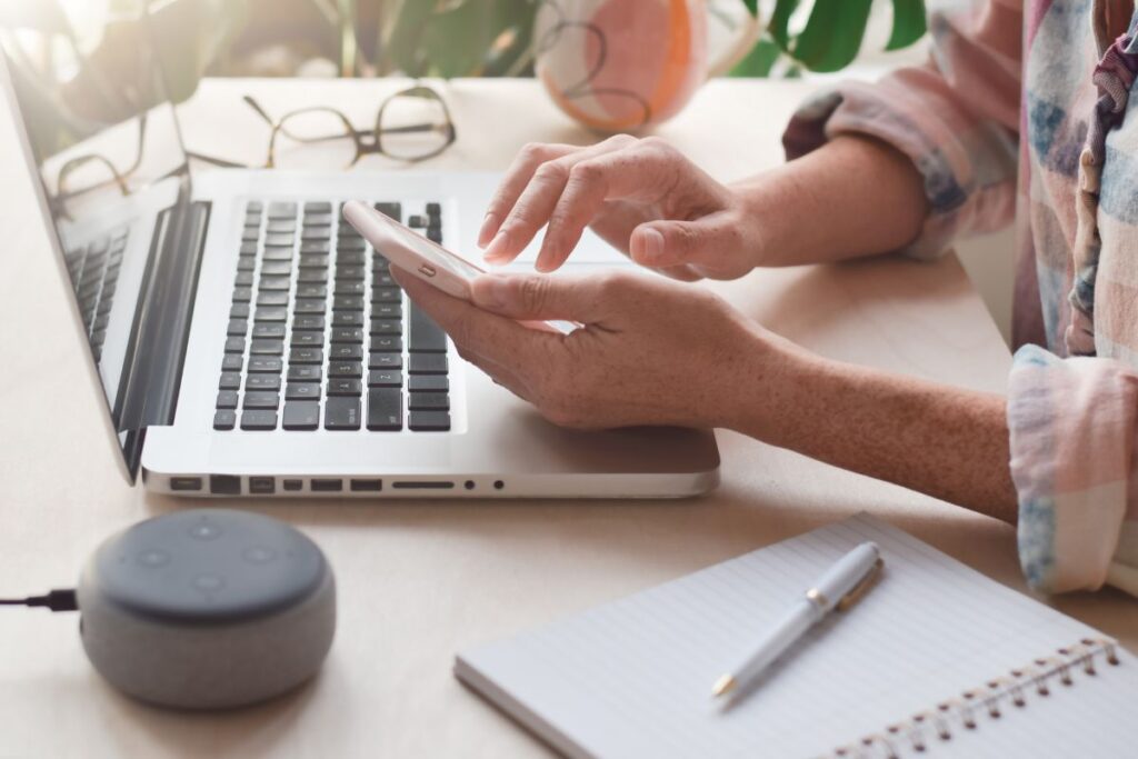 Woman typing on laptop, beside her is a voice assistant device.